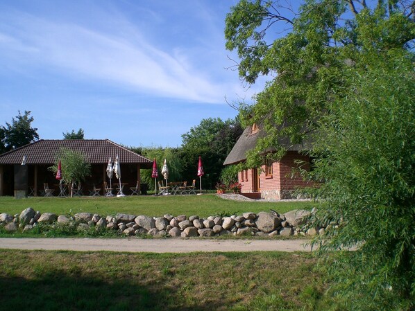 A rustic building with a tiled roof, surrounded by a stone wall and greenery. - Vacation apartment directly at the fishing pond with parking lot and terrace (Wismar)