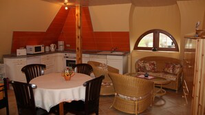 A dining area with a round table, chairs, and a wicker sofa. There is a kitchen area with a microwave, coffee maker, and cabinets. A window with an arched top is visible. - Vacation apartment directly at the fishing pond with parking lot and terrace (Wismar)