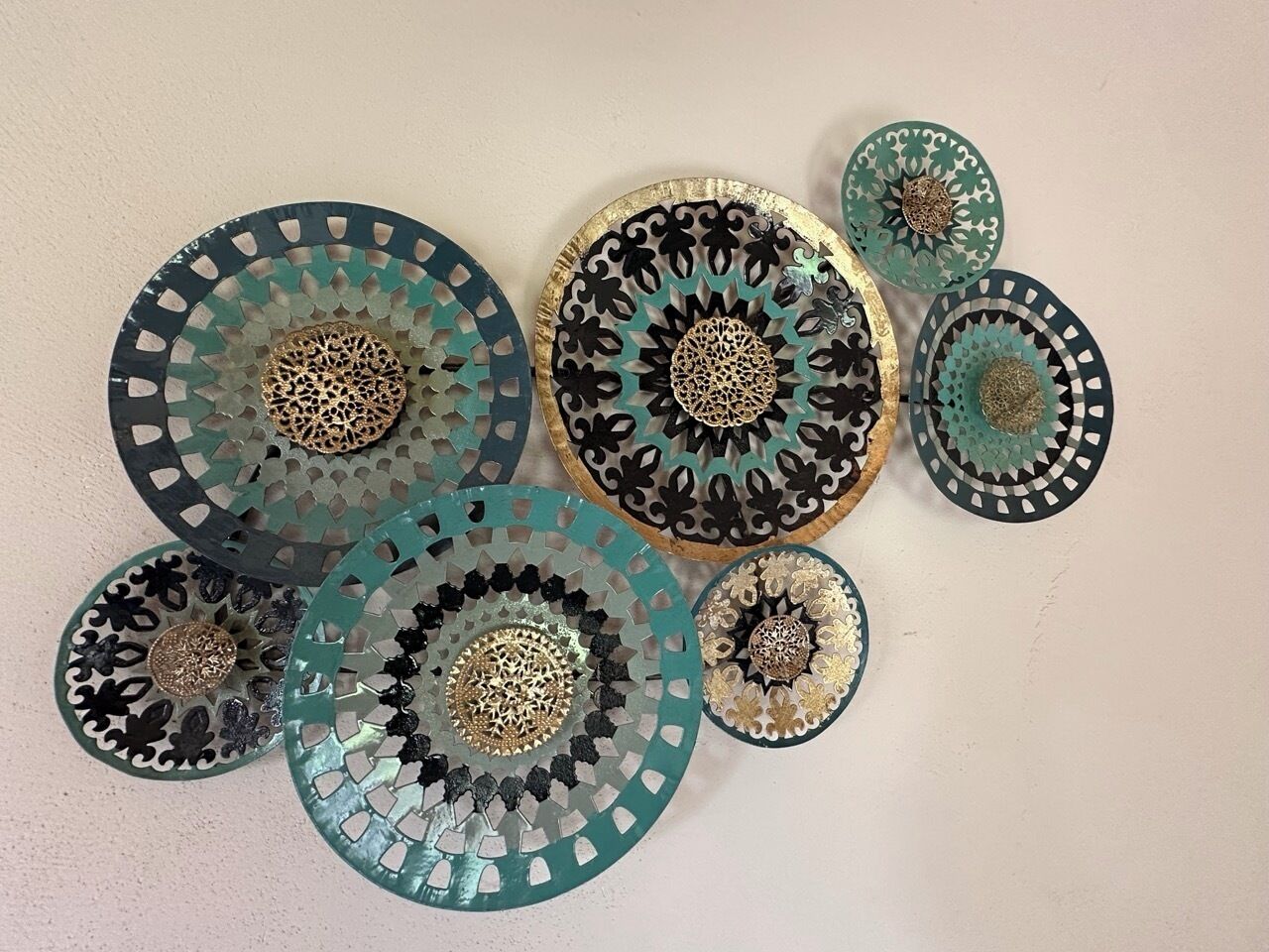 Una colección de platos decorativos con diseños intrincados y centros metálicos, dispuestos sobre una pared lisa.