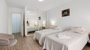 Een hotelkamer met twee bedden, een stoel, een kledingkast, een spiegel en een schilderij aan de muur.
