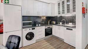 Een moderne keuken met witte kasten, een wasmachine, een magnetron en een vaatwasser.