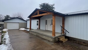 Ein eingeschossiges Gebäude mit überdachter Veranda, Garage und Betonauffahrt.