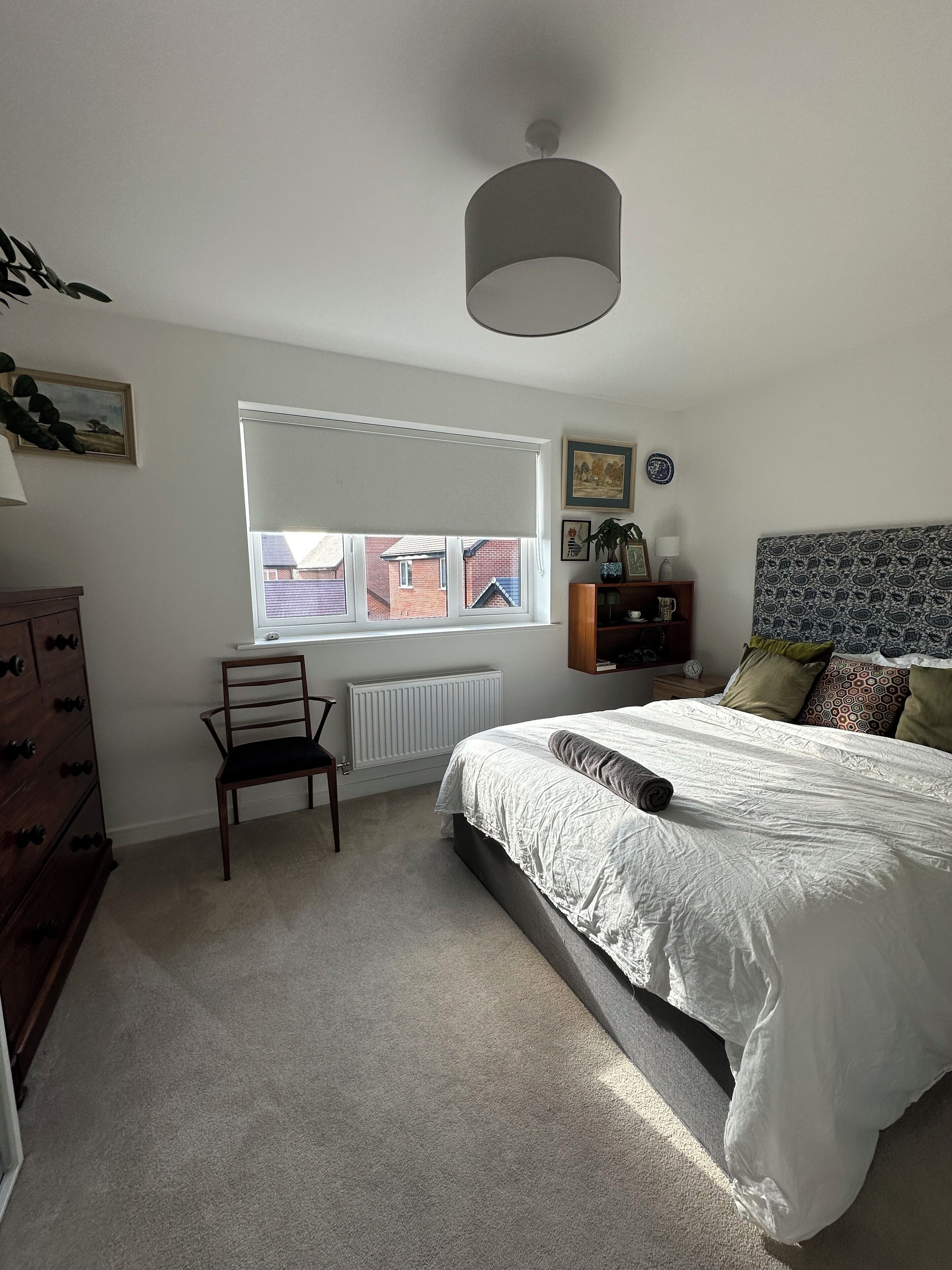 Une chambre à coucher comprenant un lit, une chaise, un radiateur, une fenêtre avec des stores et un luminaire au plafond.