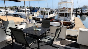 A covered outdoor seating area with a table and chairs, overlooking a marina with boats.