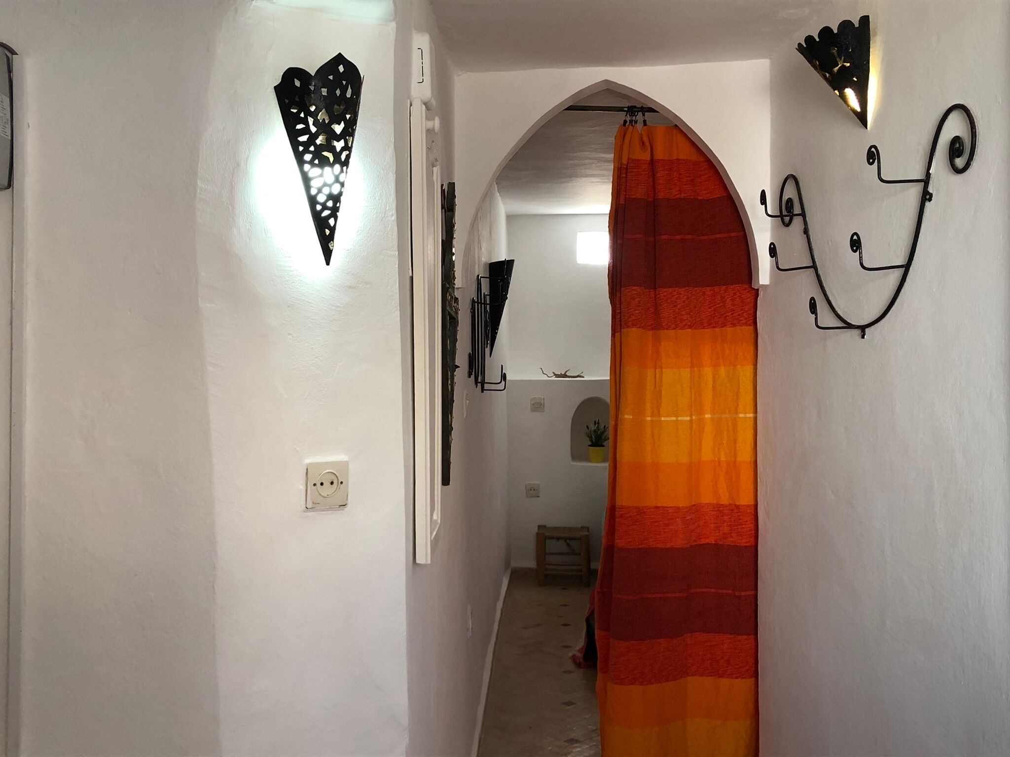 A narrow hallway with a striped shower curtain, a wall-mounted light fixture, and a decorative wall piece.