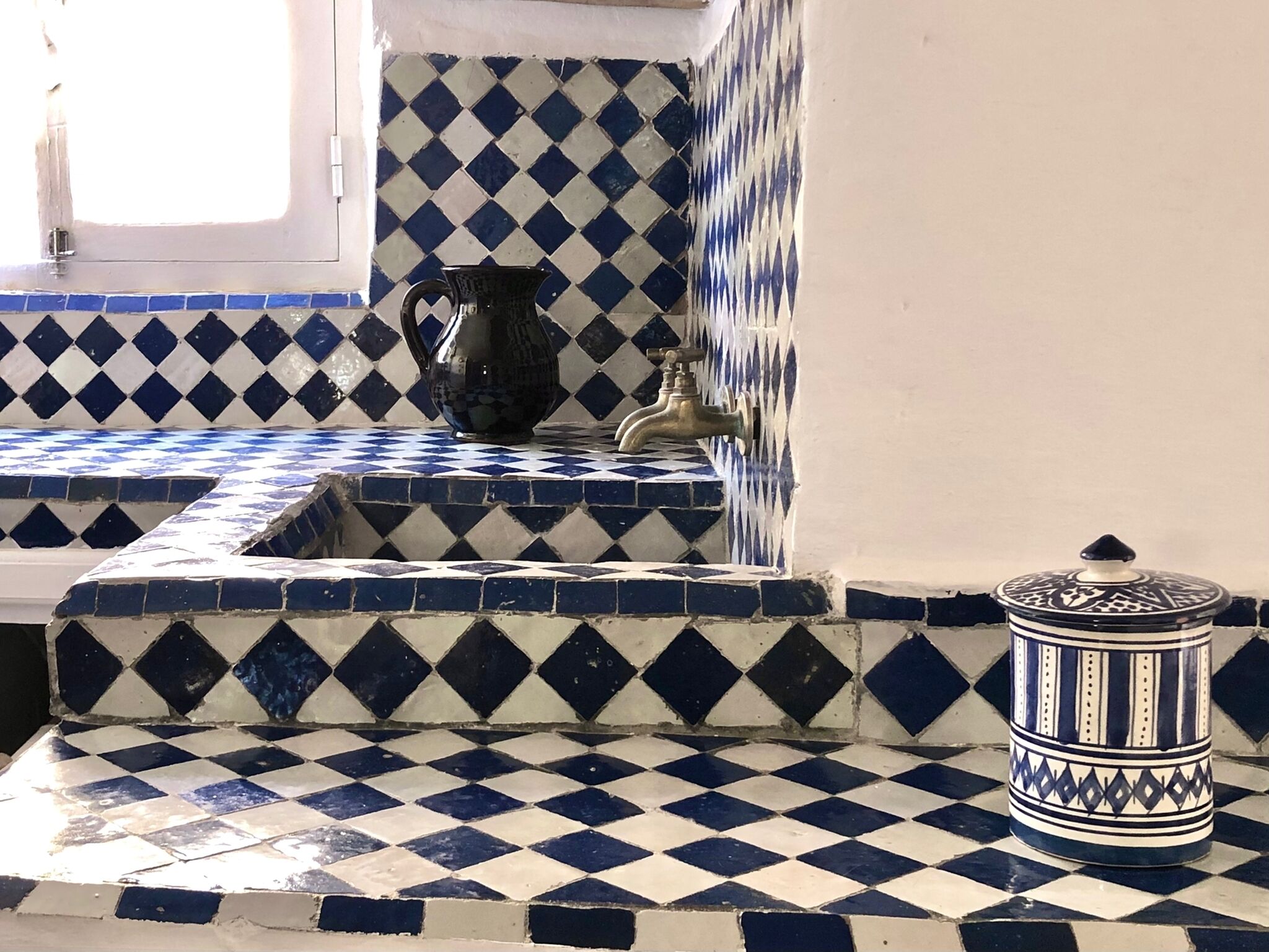 A kitchen with blue and white checkered tiles, a black pitcher, a faucet, and a patterned container.