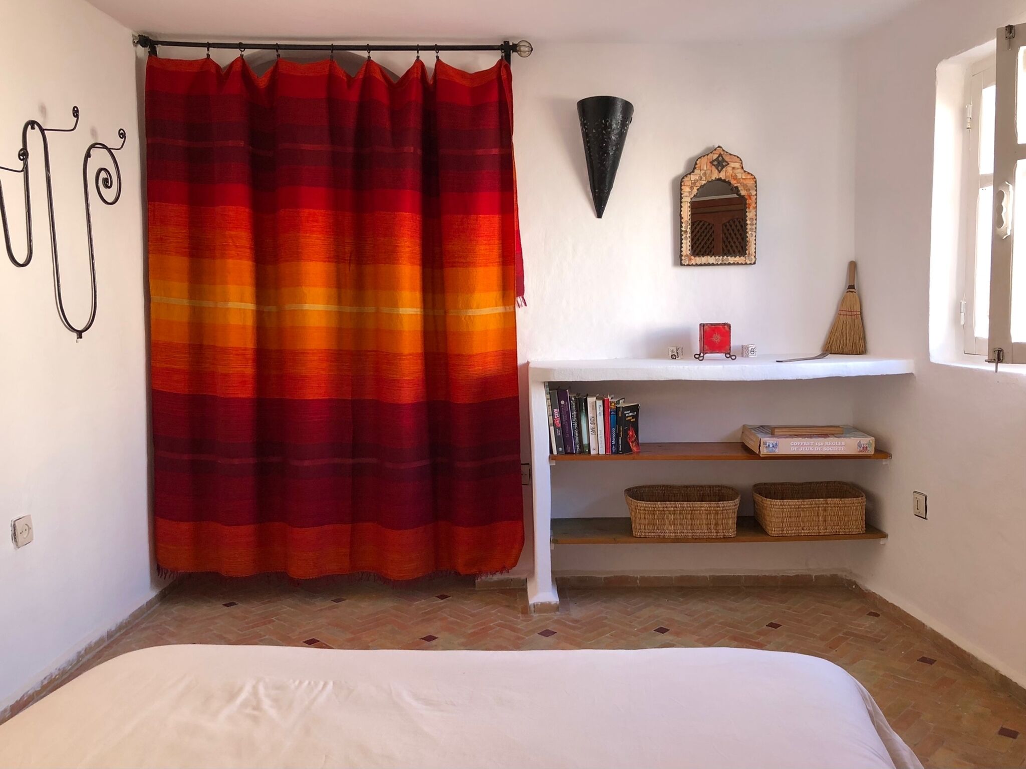 A bedroom with a bed, a bookshelf, a decorative mirror, and a window with a view.
