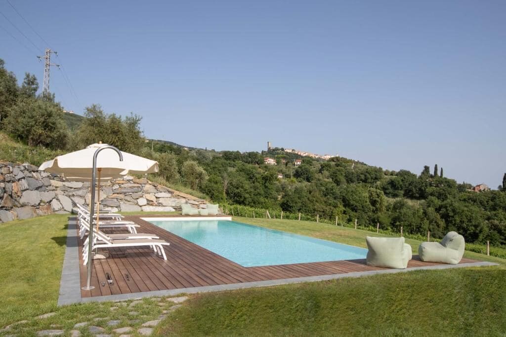 A swimming pool with lounge chairs and a deck, surrounded by greenery and hills.