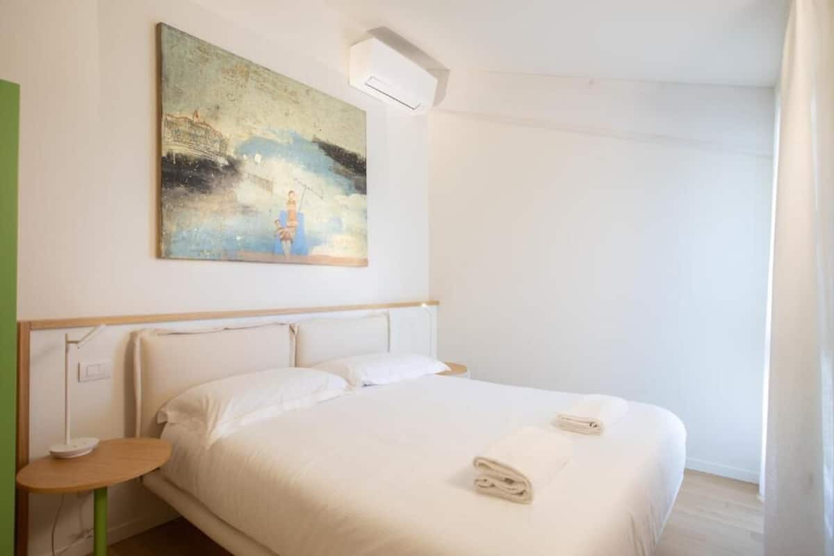 Ein Hotelzimmer mit Bett, einem kleinen Tisch, einem Bild an der Wand und einem Fenster.