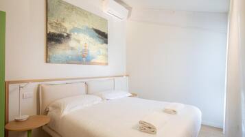 A hotel room with a bed, a small table, a painting on the wall, and a window.