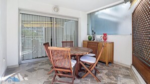 Een balkon met een eettafel en stoelen, een houten kast en een decoratieve vaas.