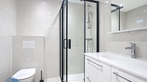 Een moderne badkamer met een douchecabine van glas, een wit toilet en een wastafel met spiegel.