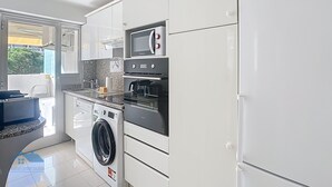 Een moderne keuken met witte kasten, een Bosch koelkast, een magnetron, een oven en een wasmachine.