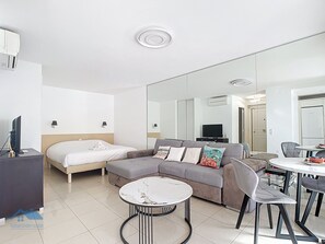 A modern hotel room with a bed, a sofa, a dining table with chairs, a TV, and a large mirror. - Spacious studio with terrace (Cannes)