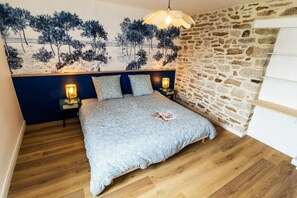 A bedroom with a bed, two bedside lamps, a stone wall, and a painting of trees. - Grand duplex 100 m² downtown Quimper - 3 bedrooms - All on foot (Quimper)