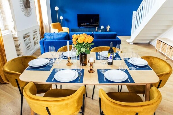 A dining area with a table set for four, blue cushions, a vase with flowers, and a television in the background. - Grand duplex 100 m² downtown Quimper - 3 bedrooms - All on foot (Quimper)
