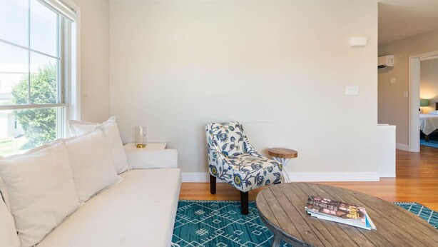 A modern living room with a white sofa, a patterned armchair, a round wooden coffee table, and a blue patterned rug. - 5BR/5BA Beachside Newport Home Steps to Beach! (Middletown)