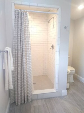 Dusche mit Glastür, Toilette und Handtuchhalter.