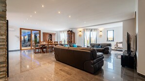 Een ruime woonkamer met een grote bank, een eettafel en een keuken op de achtergrond.