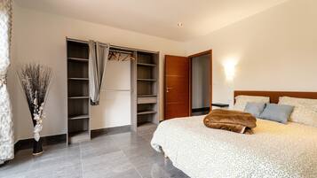 A bedroom with a bed, a wardrobe, a mirror, and a vase with dried plants.
