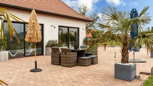 Een terras met rieten meubels, een rieten parasol en een palmboom.