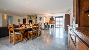 Een ruime woonkamer met een eettafel, stoelen, een stenen openhaard en een keuken op de achtergrond.