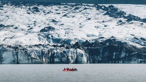 Ein Gletscher mit einer Gruppe von Menschen in einem roten Schlauchboot.