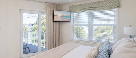 A bedroom with a bed, a window with blinds, a ceiling fan, and a view of a balcony.
