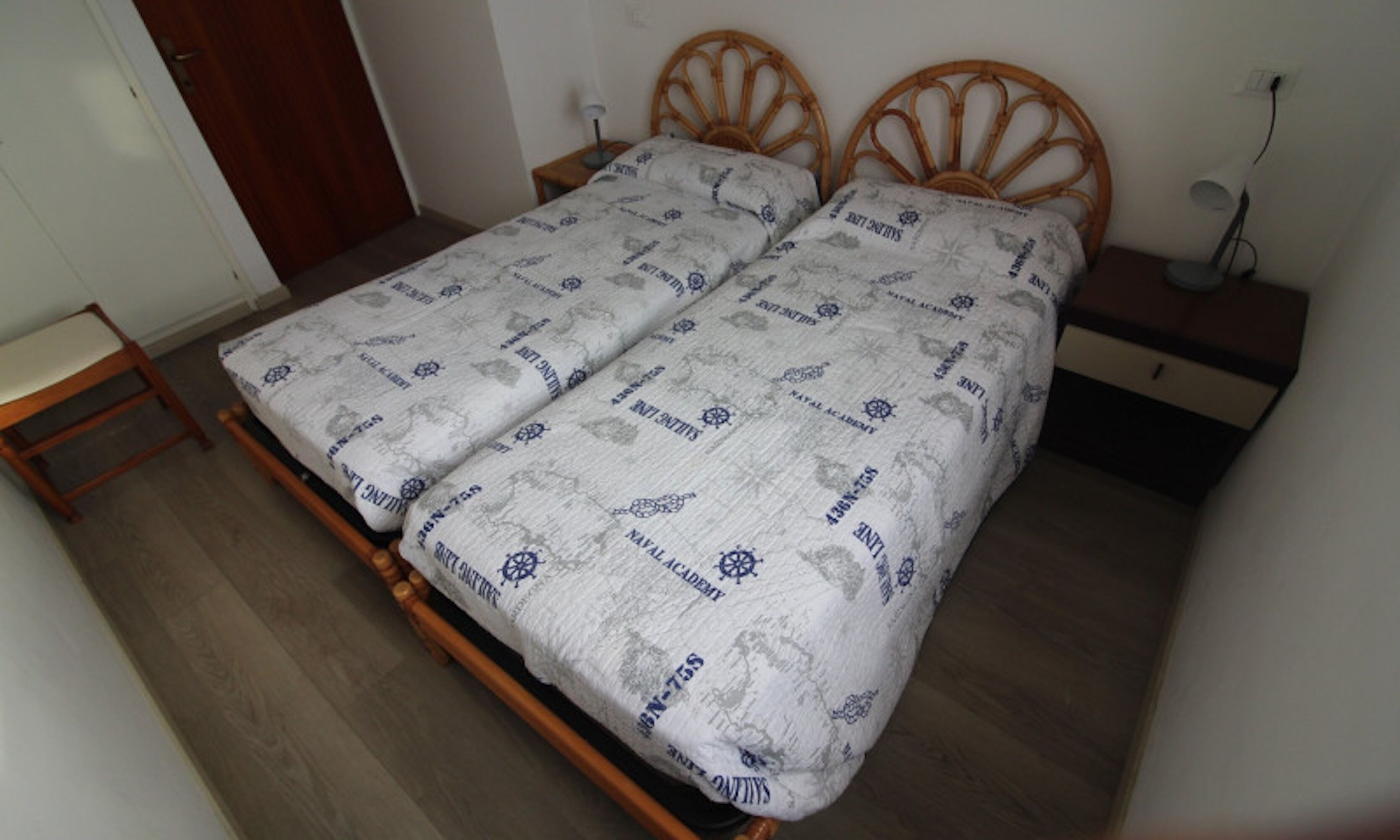 Una cama doble con colcha estampada, cabecera de madera, mesita de noche y velador.