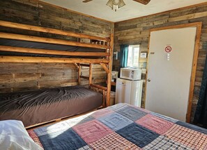 A bunk bed room with a quilt, a microwave, and a door with a no smoking sign. - Bunk Bed, Queen Bed Camping Cabin with nearby Bath House (Fancy Gap)