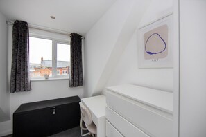 Une chambre avec une commode blanche, un banc noir et une fenêtre avec des rideaux.