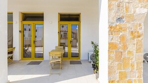 Un espacio al aire libre techado con una mesa, sillas, un muro de piedra y una puerta con marco amarillo.