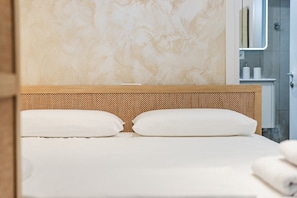 Un lit avec une tĂȘte de lit en bois, des oreillers blancs et un mur Ă motifs derriĂšre.