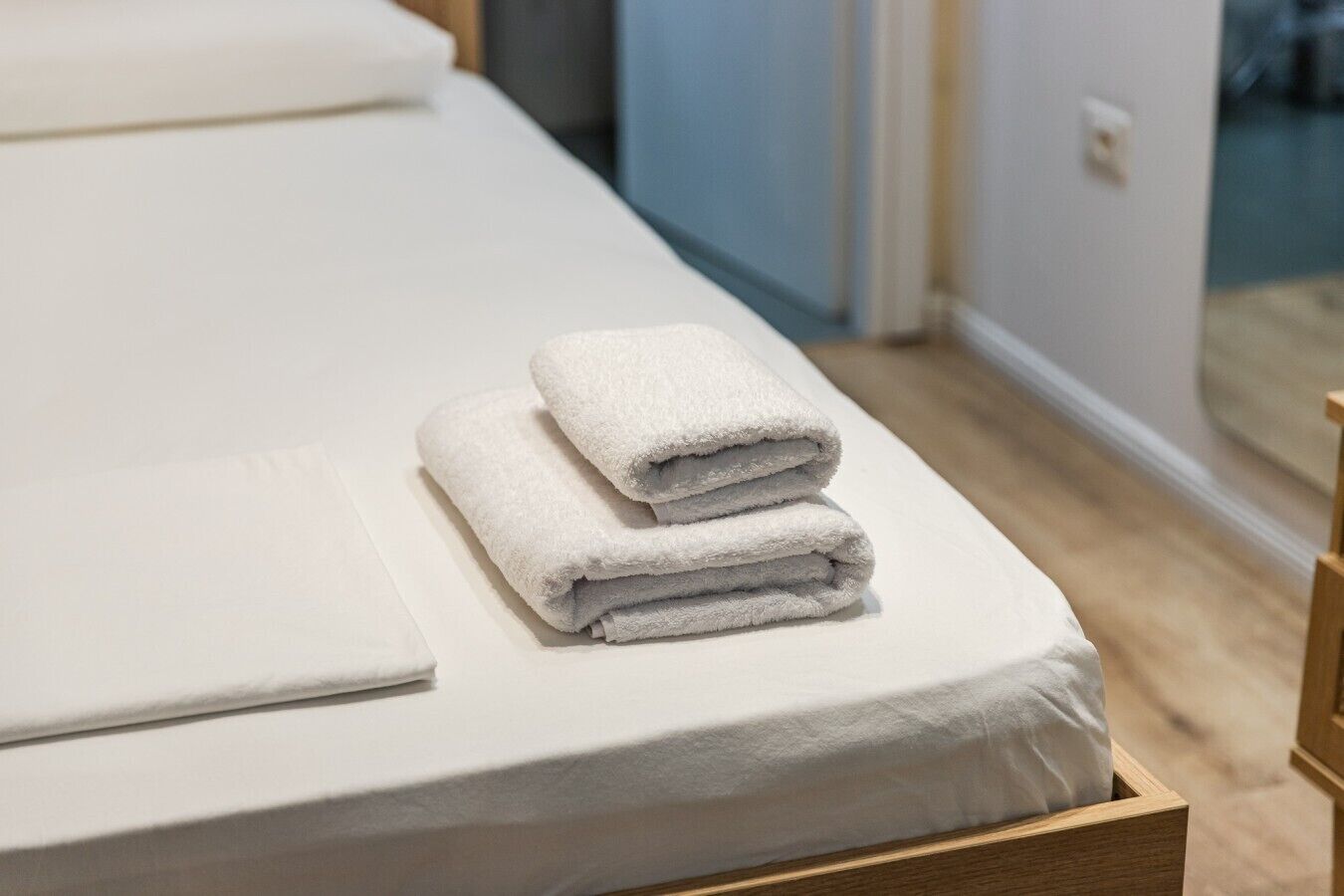 A neatly made bed with a white mattress and two folded white towels.