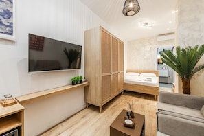 Une chambre moderne comprenant un lit, une télévision, une armoire en bois, une petite table avec une plante et un canapé.