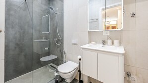 Un baño moderno con ducha envuelta en vidrio, inodoro, lavamanos con espejo y barra para toallas.