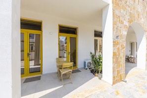 Un espace extĂ©rieur abritĂ©, dotĂ© de portes Ă cadre jaune, dâune table avec des chaises et de plantes en pot.