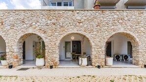 A stone building with three arched openings, potted plants, and air conditioning units. - NooN Apartment Sofo Duni | Beachside Studio in Dhërmi by PikHost (Dhërmi)