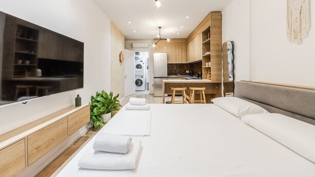 A modern hotel room with a large bed, a TV, a kitchenette, and a laundry area. - NooN Apartment Sofo Duni | Beachside Studio in Dhërmi by PikHost (Dhërmi)