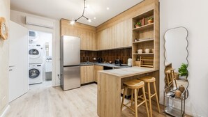 A modern kitchen with wooden cabinets, a built-in island with stools, a coffee machine, and a refrigerator. - NooN Apartment Sofo Duni | Beachside Studio in Dhërmi by PikHost (Dhërmi)