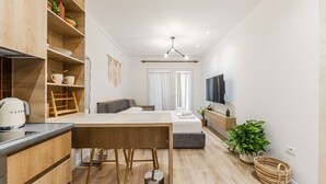A modern, compact living space with a kitchenette, a dining area, a sofa, a TV, and a potted plant. - NooN Apartment Sofo Duni | Beachside Studio in Dhërmi by PikHost (Dhërmi)