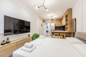 Habitació d'hotel moderna amb un llit gran, televisió, zona de cuina petita i rentadora.