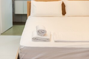 A neatly made bed with white linens and a rolled towel on the side. - NooN Properties | 3 by PikHost (Dhërmi)