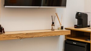 Ein modernes Zimmer mit einem an der Wand befestigten Flachbildfernseher, einem kleinen Holztisch mit blauem Stuhl, einer Kaffeemaschine und einem Breville Mini-Kühlschrank.