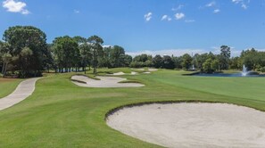 En golfbana med sandbunkrar, ett vattendrag och träd.