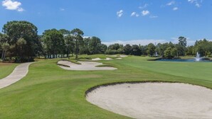 Ein Golfplatz mit Sandbunkern, einem Wasserspiel und Bäumen.