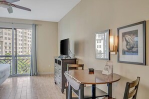 A hotel room with a balcony, a dining table, a TV, and artwork on the walls. - Studio In Sandestin's Baytowne With Superb View (Miramar Beach)