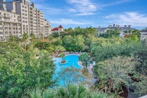 A hotel with a swimming pool surrounded by lush greenery and a red-roofed building in the background. - Studio In Sandestin's Baytowne With Superb View (Miramar Beach)