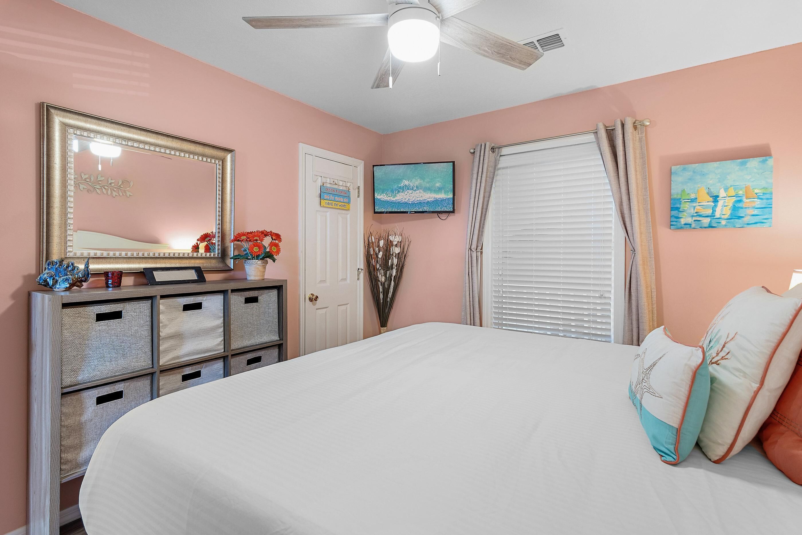 A bedroom with a bed, dresser, mirror, television, and artwork.