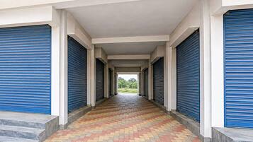 A covered corridor with blue shutters, tiled flooring, and steps leading to an open area.
